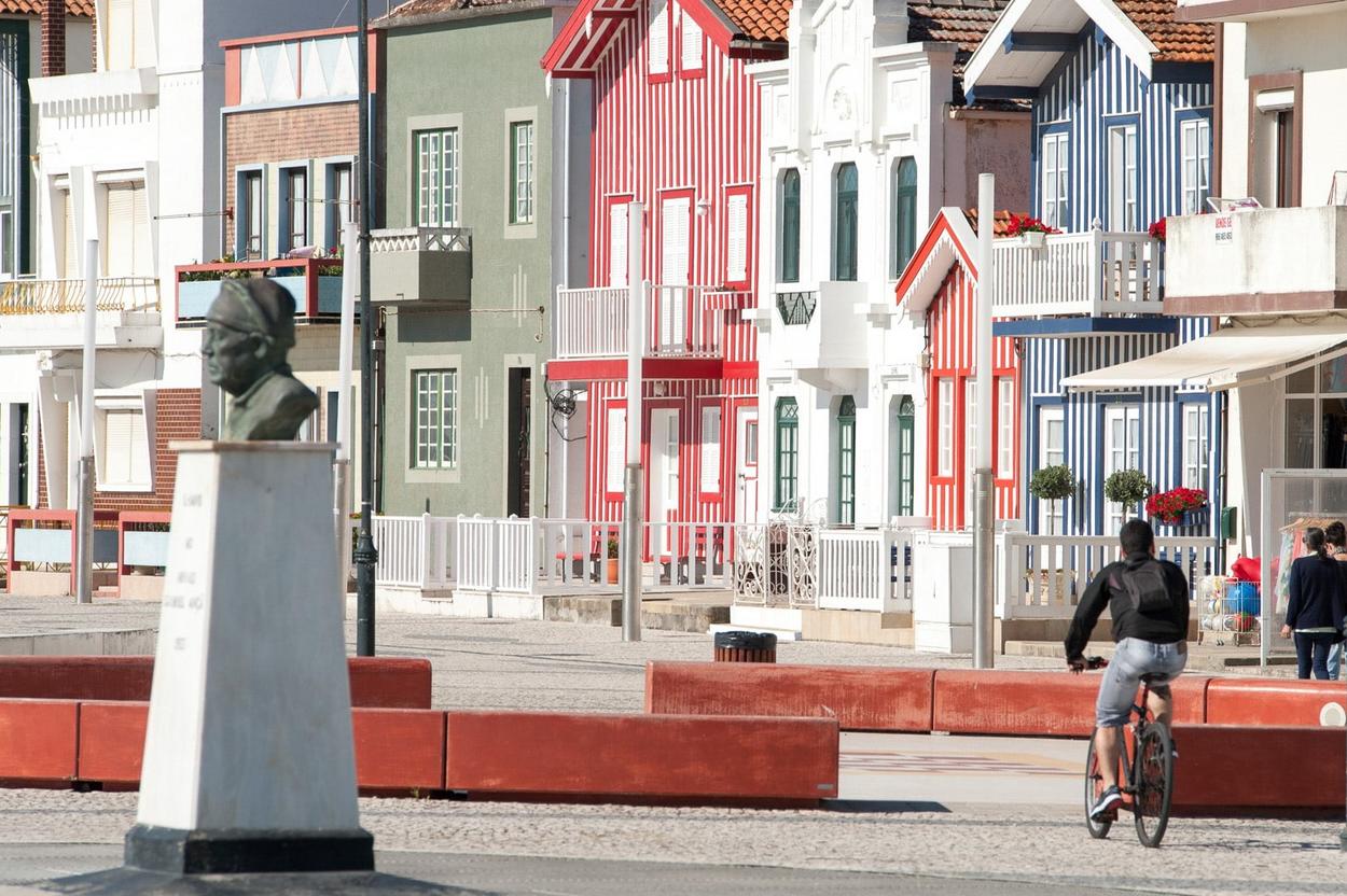 fotografia da calçada arrais ançã com um ciclista, o busto do arrais ançã e, ao fundo as casas típicas da costa nova chamadas palheiros
