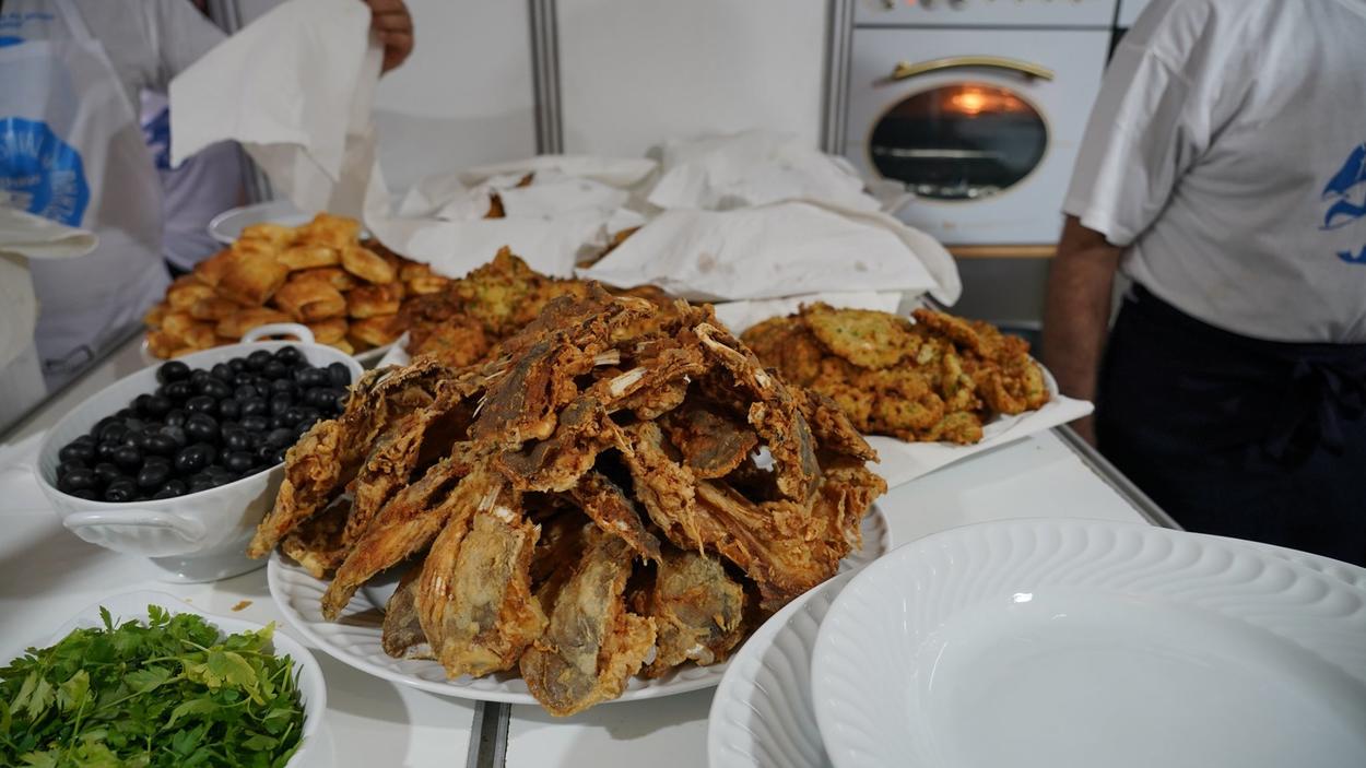 Cozinha no Festival do bacalhau onde se vêem caras de bacalhau fritas, azeitonas pretas, salsa e pataniscas